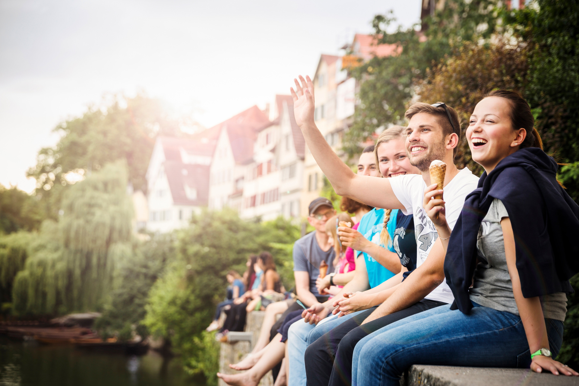 students sitting on a a wall at a river with waving hands