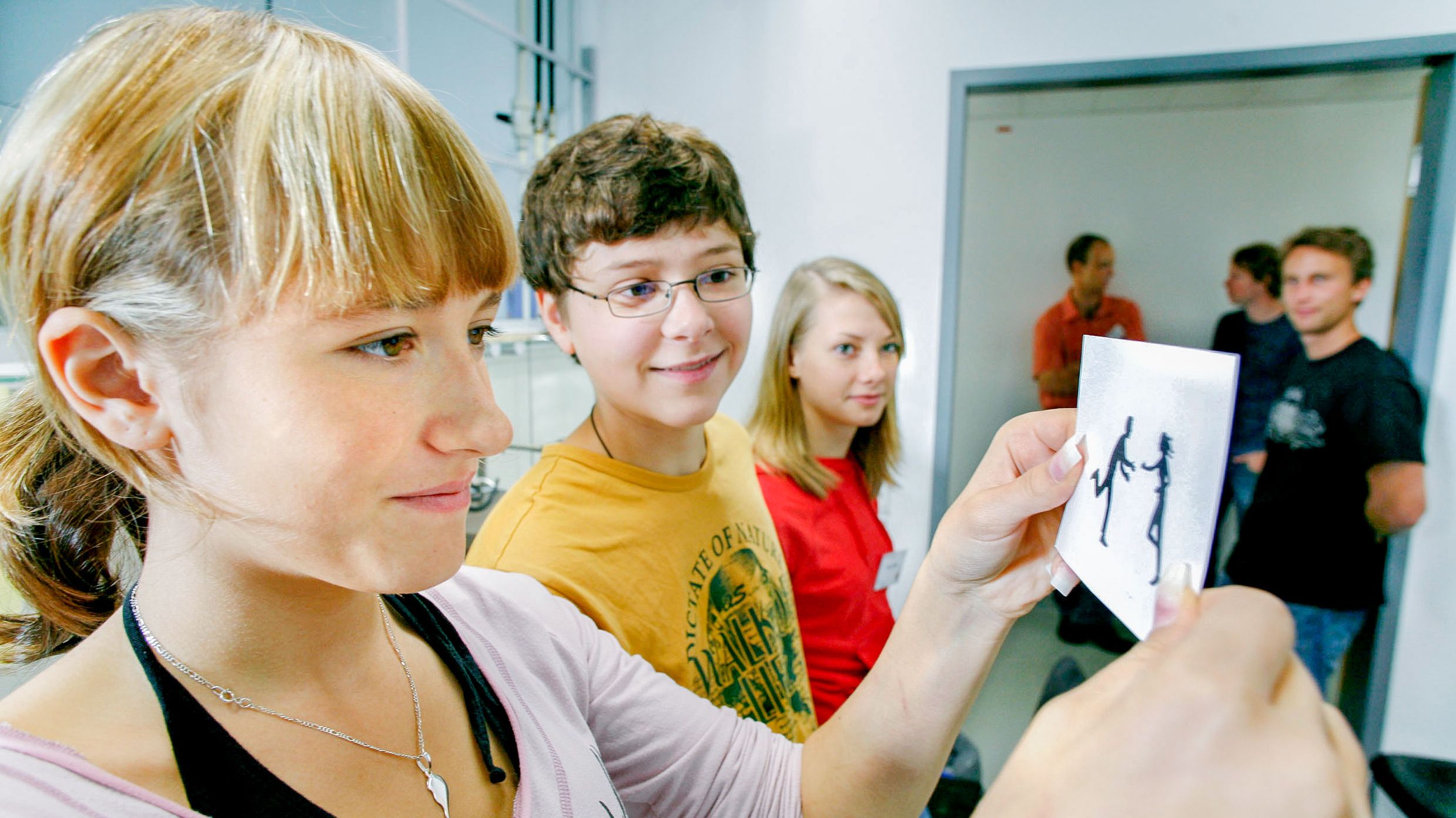 Several pupils are standing in a seminar room, the girl in the foreground is looking at a black and white drawing.